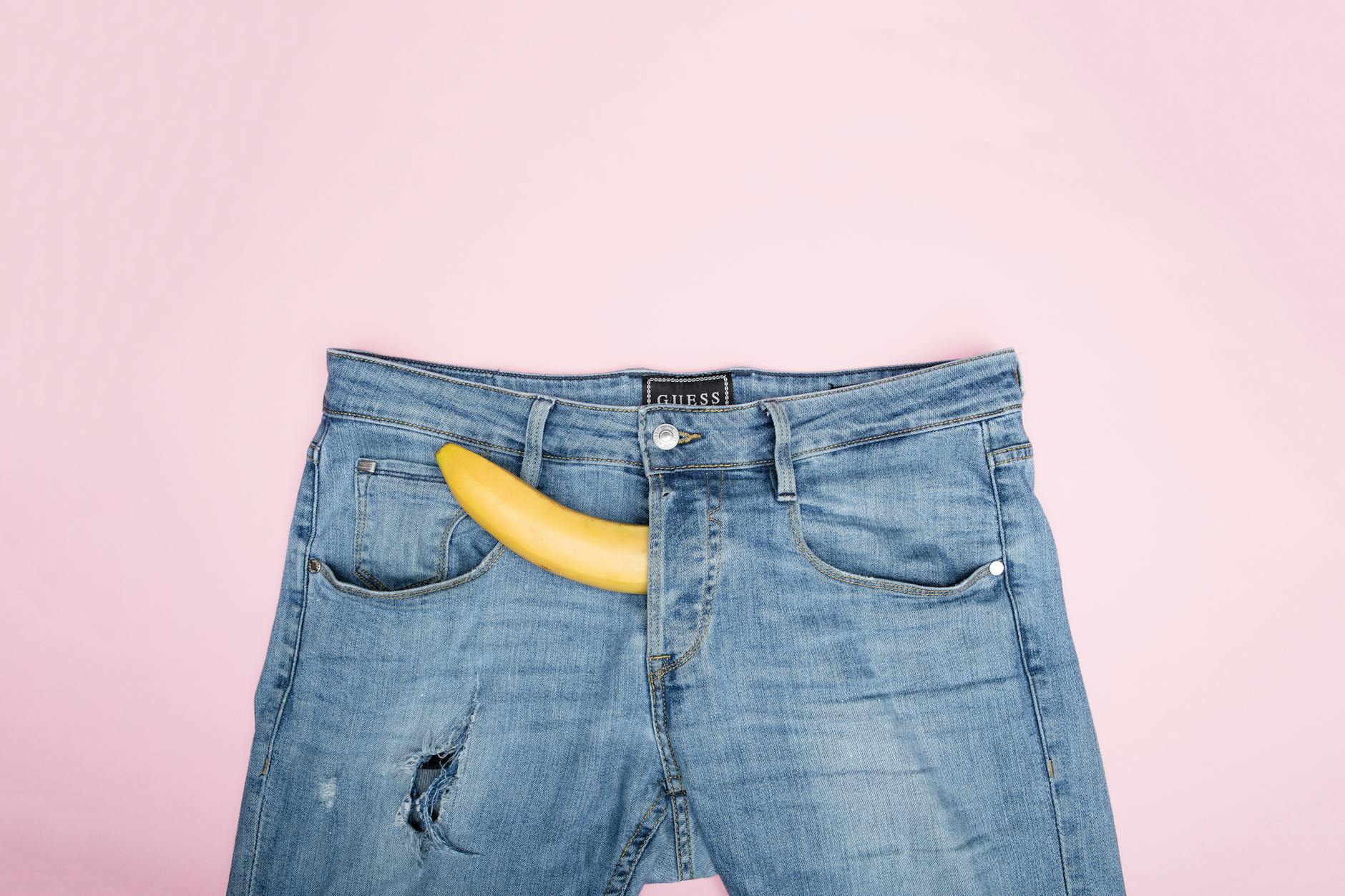 Fun and conceptual still life photo featuring a banana in blue jeans against a pink background.